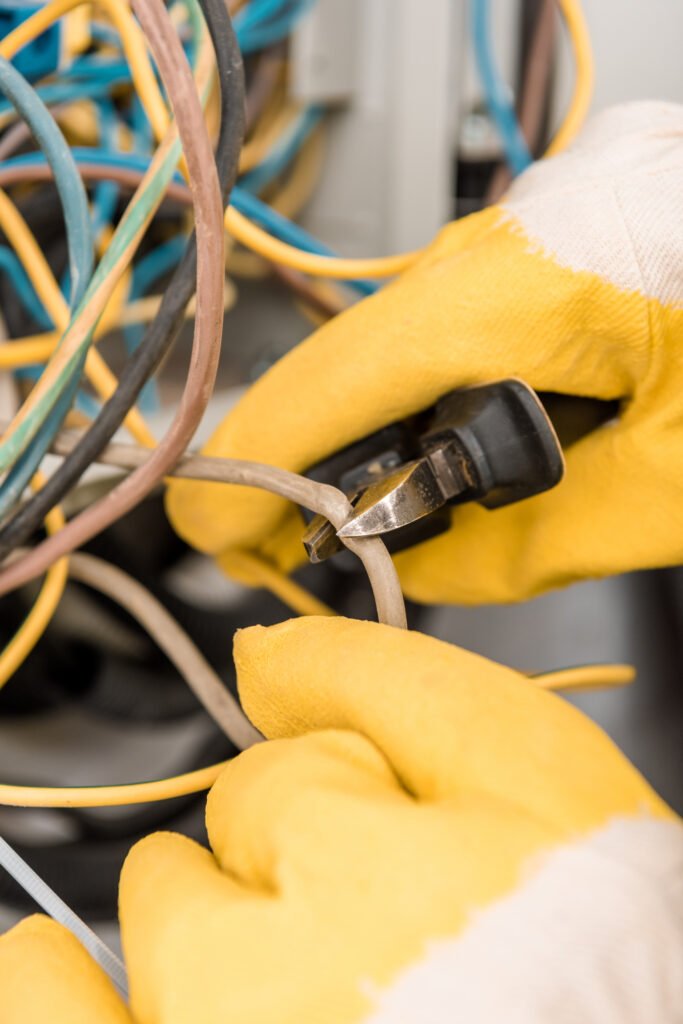 cropped image on electrician cutting wires from electrical box with pliers in corridor